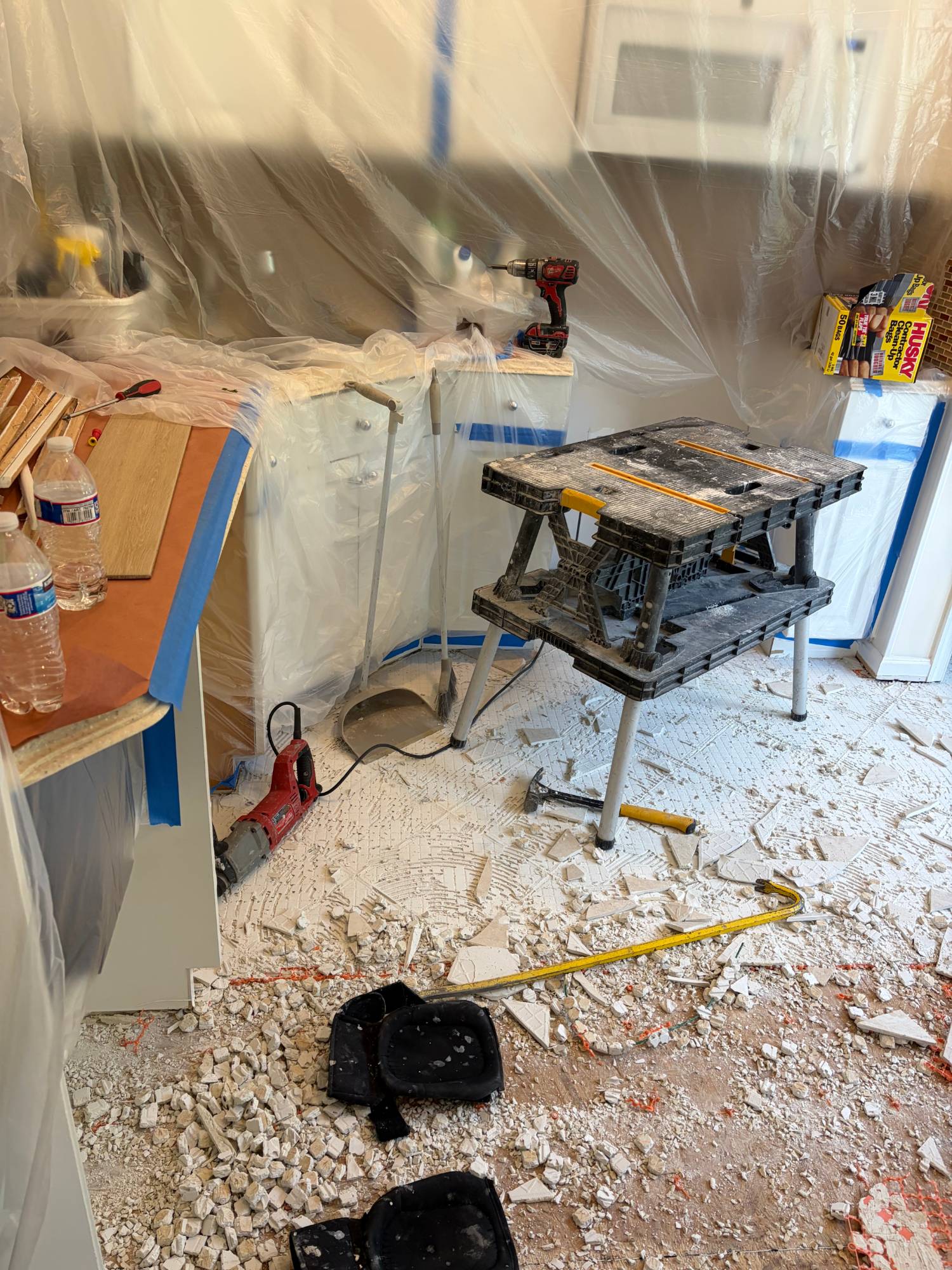 Kitchen before — old tile removed, cabinets protected with plastic sheeting during demolition